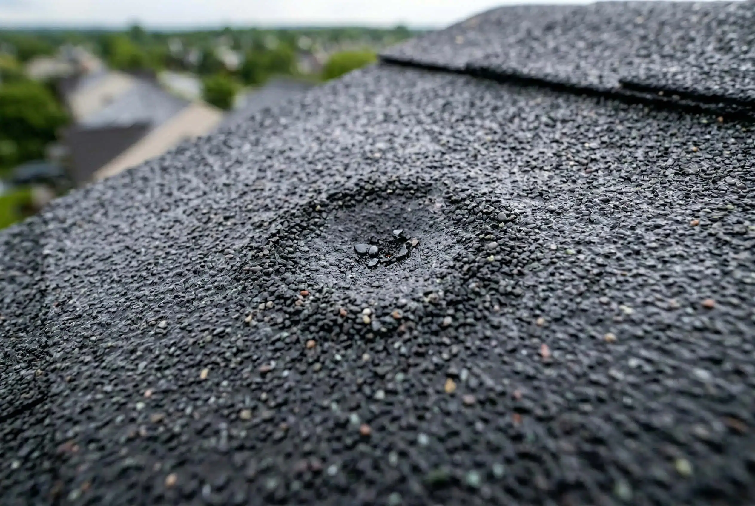 Close-up of subtle hail bruising on asphalt shingles — damage invisible from the ground